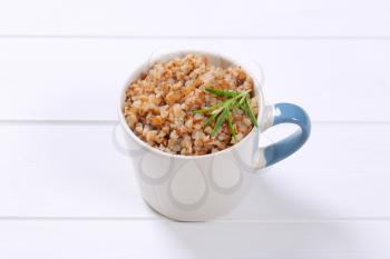 mug of cooked buckwheat on white wooden background