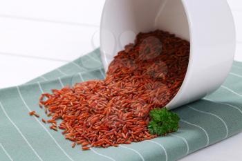 bowl of red rice spilt out on grey place mat - close up