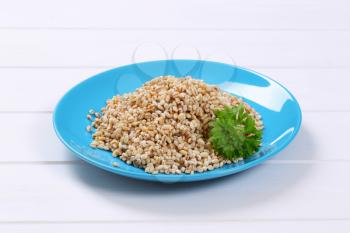 plate of cooked pearl barley on white wooden background