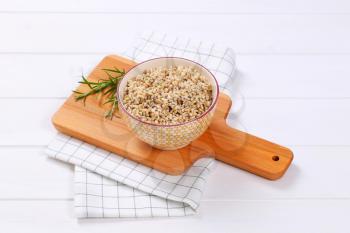 bowl of cooked pearl barley on wooden cutting board