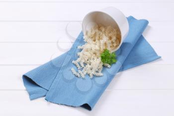 bowl of cooked rice pasta fusilli spilt out on blue place mat