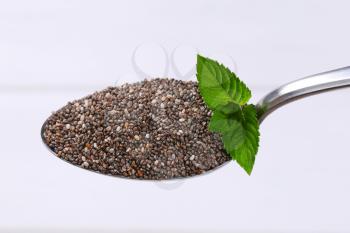 spoon of chia seeds on white wooden background