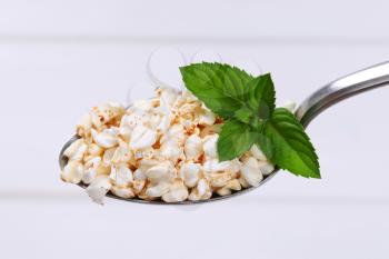 spoon of puffed buckwheat on white wooden background