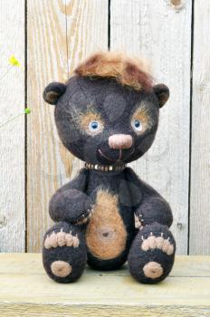 Handmade, the sewed toys: teddy-bear Mocca on a wooden bench against wooden boards