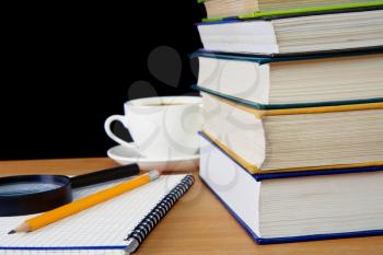 pile of books, pencil on notebook and cup of coffee on table