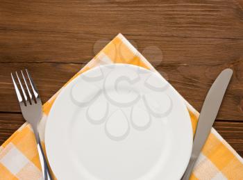 plate, knife and fork at napkin on wooden background