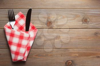 knife and fork in napkin at rustic wooden plank board table background, top view
