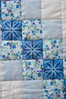Embroidered by dark blue and white patterns a scrappy blanket.