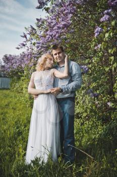 Newly-married couple among lilac bushes.