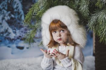 The child is sitting in the snow under the tree.