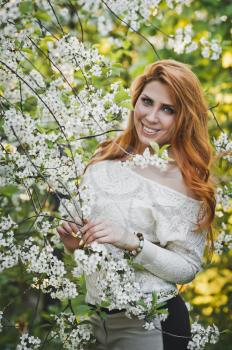 Portrait of a girl with red hair among the flowers of cherry and Apple trees.