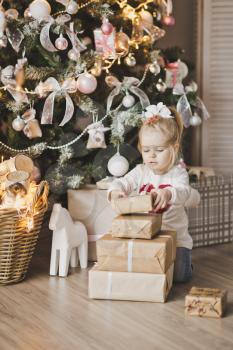 Little girl sitting under the Christmas tree with gifts.