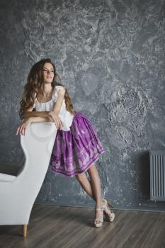 A life-size portrait of a girl in a skirt and with long hair on grey background textured wall.
