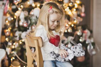 Little girl sitting near Christmas tree in expectation of a miracle.