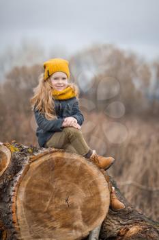The child is sitting on the felled trunk of a large tree.