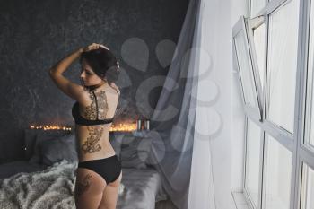 Bare back girl with a huge tattoo standing on the background lights garland.