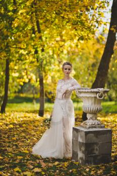 Portrait of a bride in a fitted long white dress against the background of the autumn garden.
