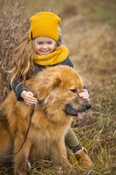 Little girl in a yellow hat and scarf, stroking the face of a huge red dog.
