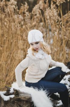 Portrait of a girl sitting in the winter on a fallen tree in the reeds by the lake.