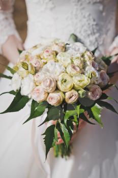 A neat bouquet of pink and yellow rose buds in women's hands.
