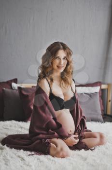 Future mother with curly hair sitting on the bed.