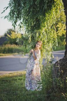 Pensive girl at the trunk of a weeping willow.
