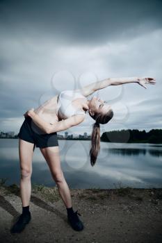 dramatic style photographs. gymnast doing exercises near the water in the evening before the storm.