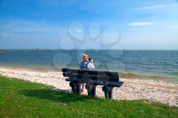 Girl on a bench enjoying the sea view and take pictures.
