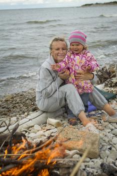 mother and daughter at the sea in the fall sitting around the campfire .