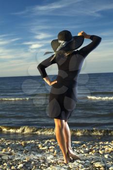 Woman in black dress walking on the sea in the evening. Photo with light effect