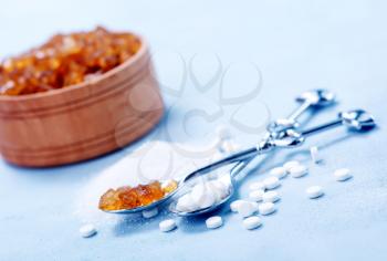 Pile of brown sugar cubes and stevia on blue wooden background