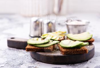 bread with avocado on board and on a table