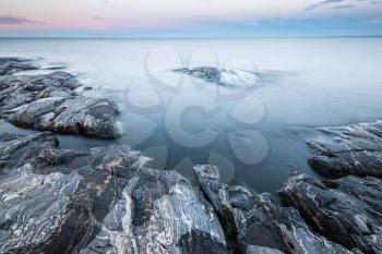 Tranquil minimalist landscape of stony coast with gray rocks and calm water under blue sky in twilight in early morning, beautiful calm natural background