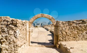Ancient arch at Bahrain Fort with Manama skyline. A UNESCO World Heritage Site in the Middle East