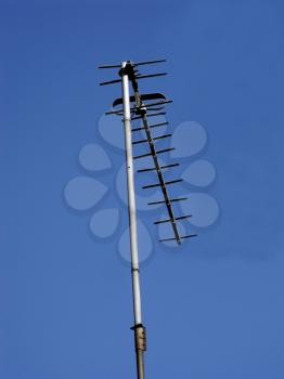 A television antenna on a mast on a background of blue sky