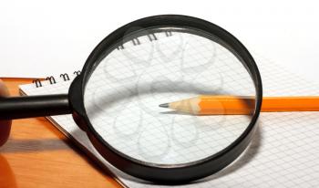 Pencil and magnifying glass on a notepad close up