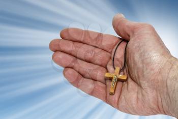 Hand with a wooden cross on a blue background with rays of light