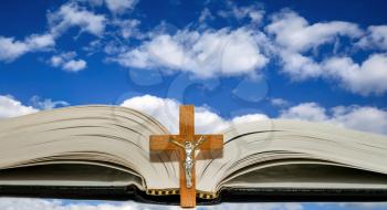 Open book with a cross against a blue sky with white clouds