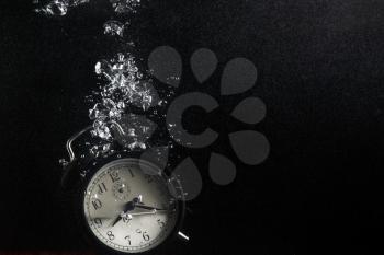 Concept of time. Vintage alarm clock in water with air bubbles. Photo on black background. Plenty of space for text.
