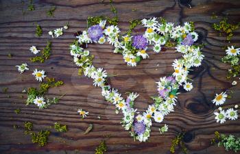 Heart symbol made of flowers on vintage wooden table background. Top view.