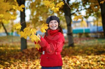 Laughing woman in a beret and red jacket on a background of yellow autumn maple leaves. Shallow depth of field. Selective focus on model.