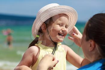 Happy laughing little girl in a white hat on the bright blurred background seascape. Selective focus on child's face.