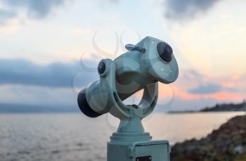 Public monocular on sea shore. Coin operated binocular viewer on blurred background of sunset and sea. Shallow depth of field. Selective focus.