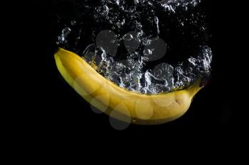 Fresh banana splash in water with air bubbles. Yellow banana in water on black background. Healthy food. Wash fruits.