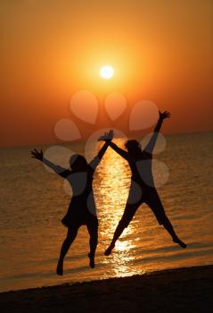 Two girls jumping on a background of the rising sun over the sea. Focus on models. Shallow depth of field. Toned image.