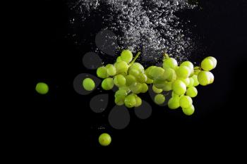 Green grapes falling into the water with air bubbles. Photo on black background. High speed photography.
