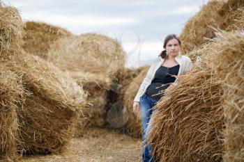 Pretty young woman in a white blouse and jeans posing on the background of haystacks. Rural scene.