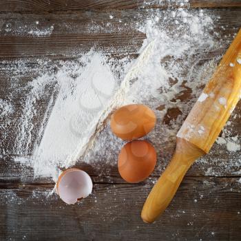 Cooking background with eggs, eggshells, flour and rolling pin.