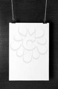 Blank white paper poster hanging on dark background. For design presentations and portfolios. Front view.