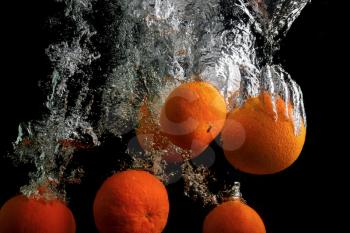 Tangerines fall in the water with air bubbles. Washing fruits. Photo on a black background.